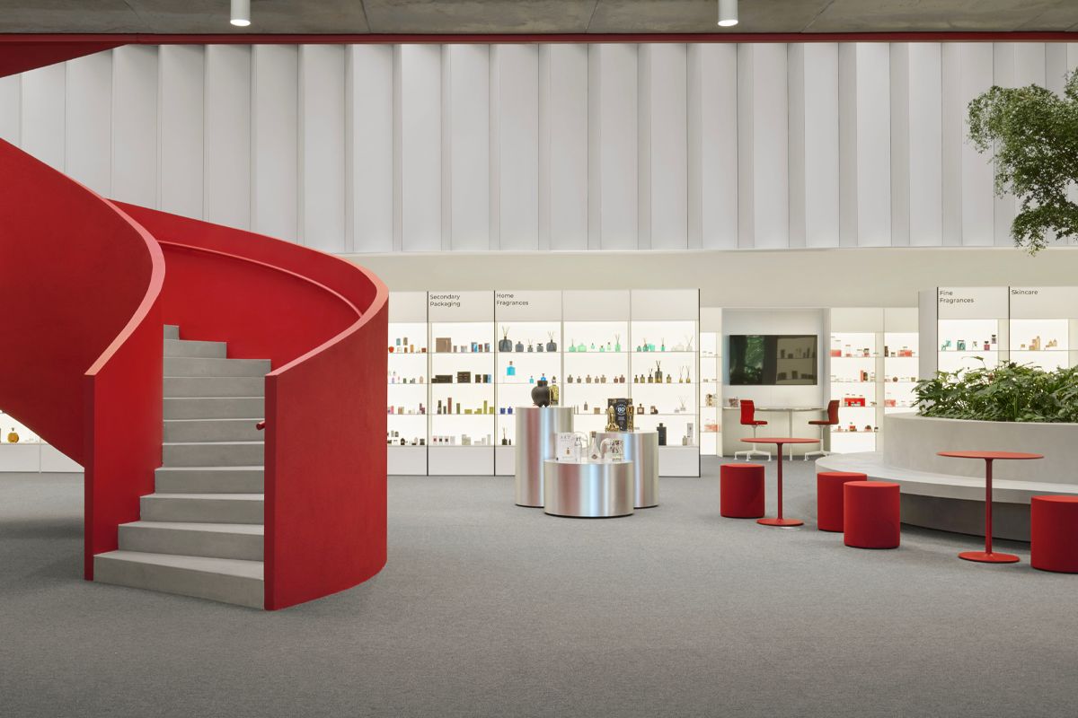 Modern interior with a red spiral staircase, display shelves with products, red seating and tables, and a plant area under soft lighting.