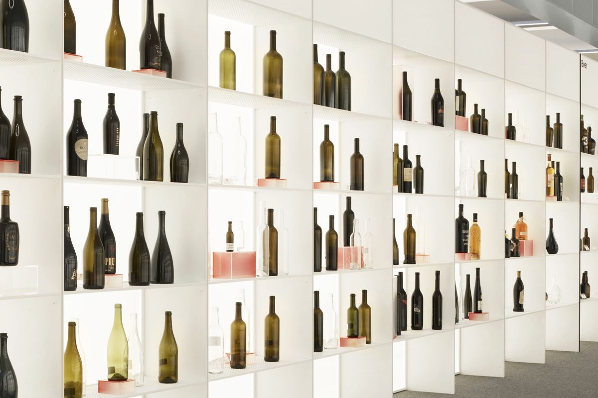 Rows of various wine bottles displayed on illuminated white shelves, creating a visually striking pattern.