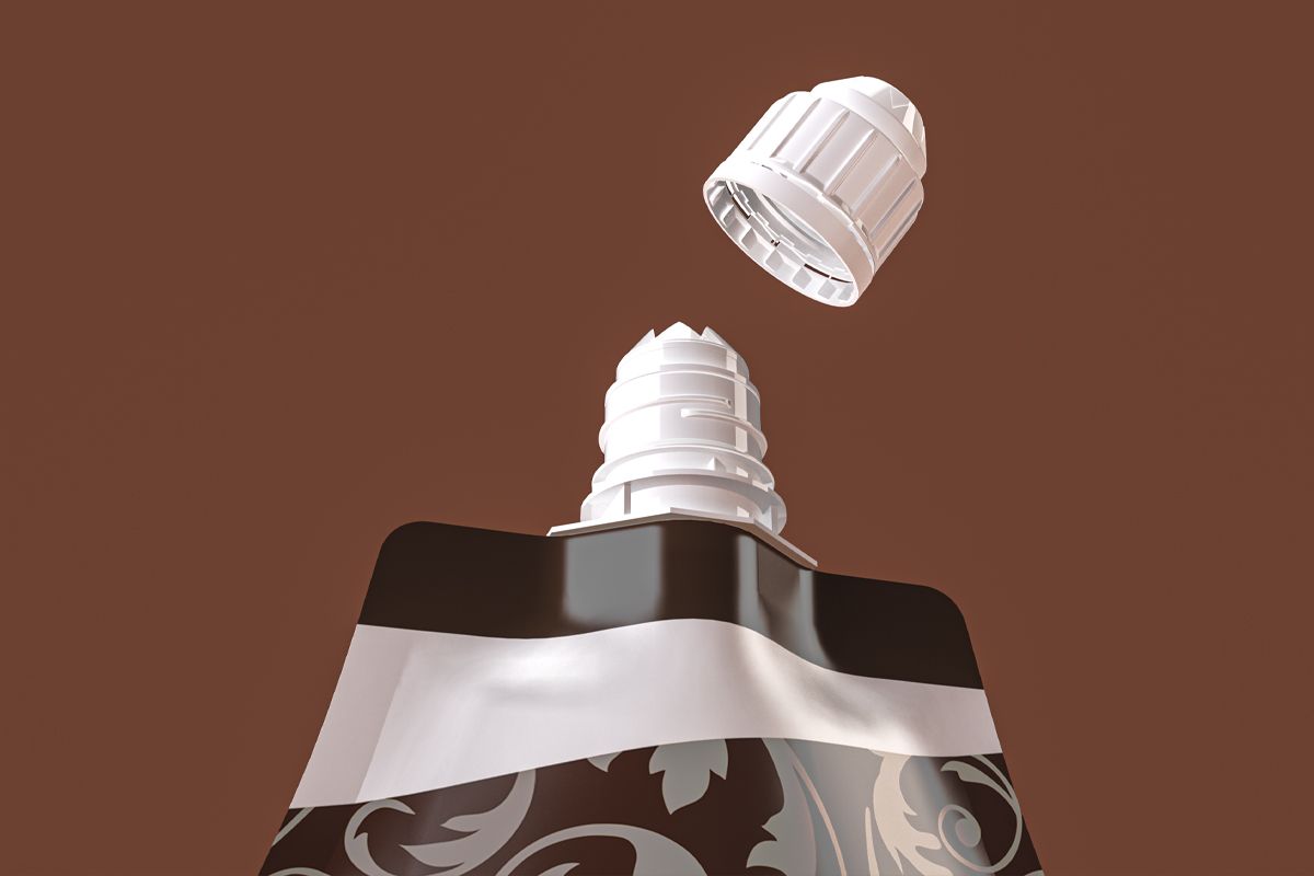 Close-up view of a spout pouch with a decorative brown and beige design, showing the white screw cap detached above the spout opening against a solid brown background. Close-up view of a spout pouch with a decorative brown and beige design, showing the white screw cap detached above the spout opening against a solid brown background.