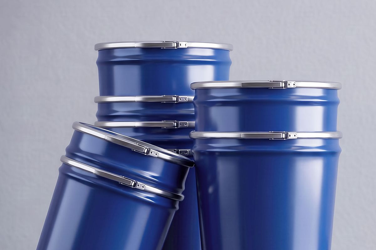 Four blue metal drums with silver lids arranged closely together against a light gray background.