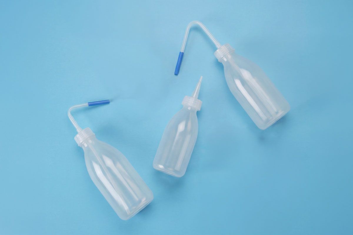 Three clear plastic wash bottles with blue nozzles on a blue background, arranged in a scattered formation.
