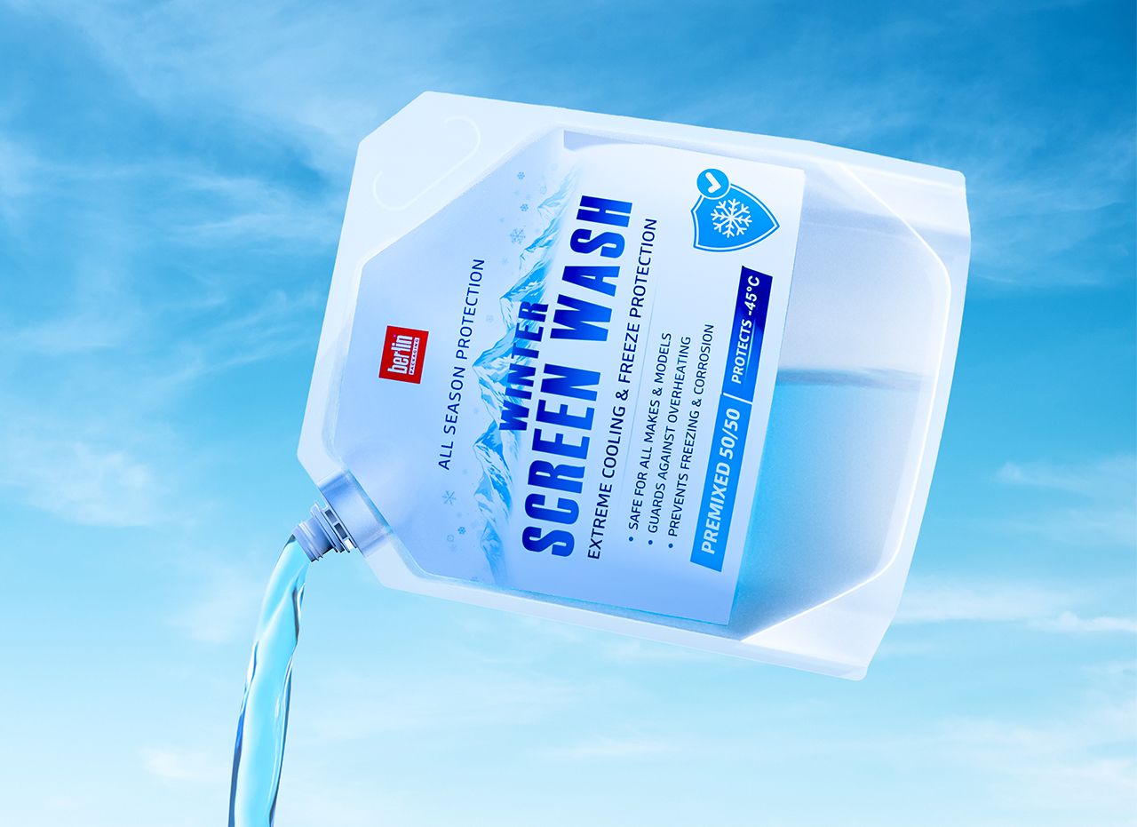 A clear jug of screen wash being poured, labeled for extreme cooling and freeze protection, with snowflake graphics, against a blue sky.