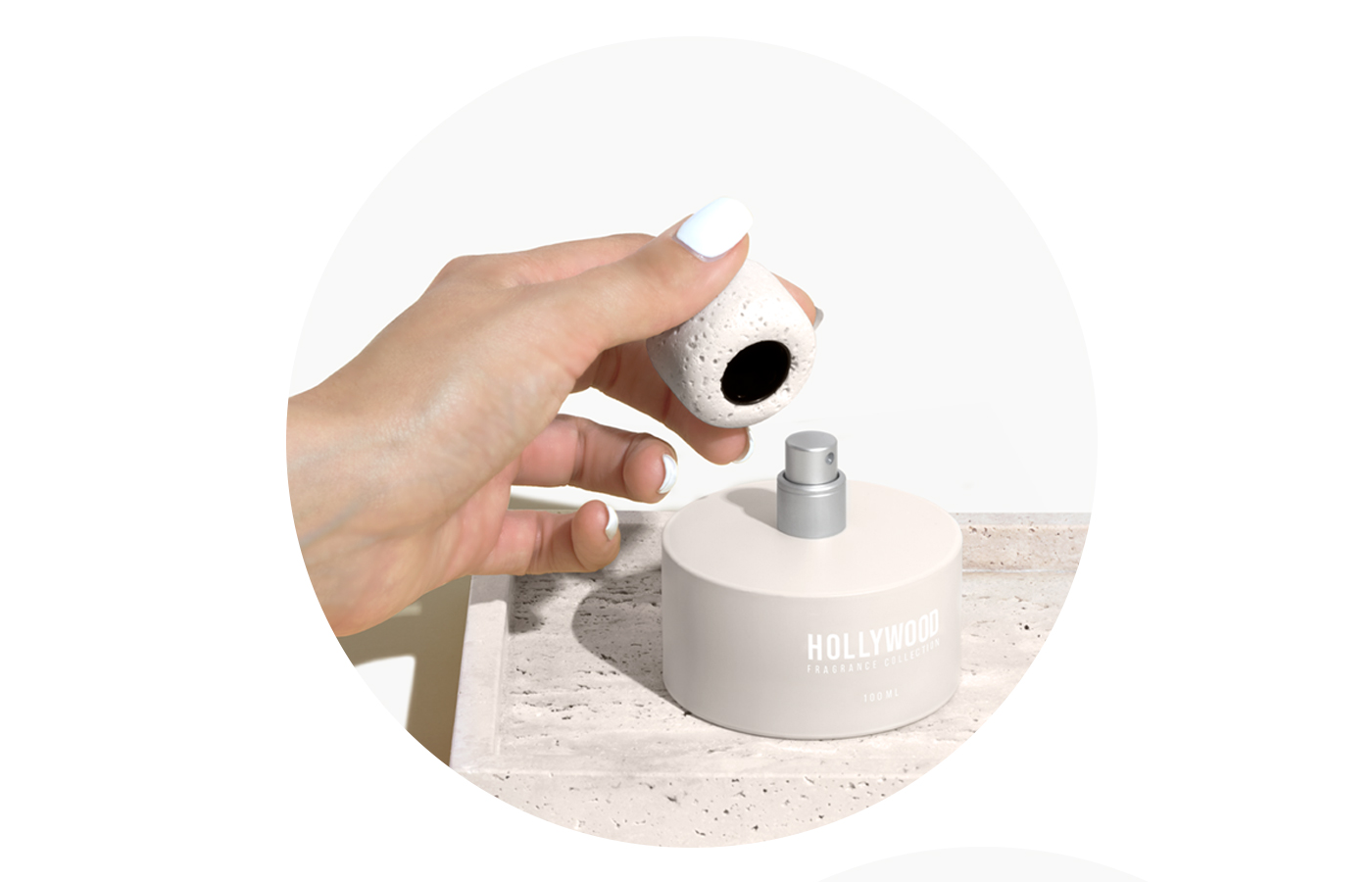 BP_EM_INTERNATIONAL_NEWS_HOLLYWOOD_STEP1 Hand removing stone-textured cap from Hollywood Fragrance Collection perfume bottle on marble surface. Modern and sustainable fragrance packaging concept.