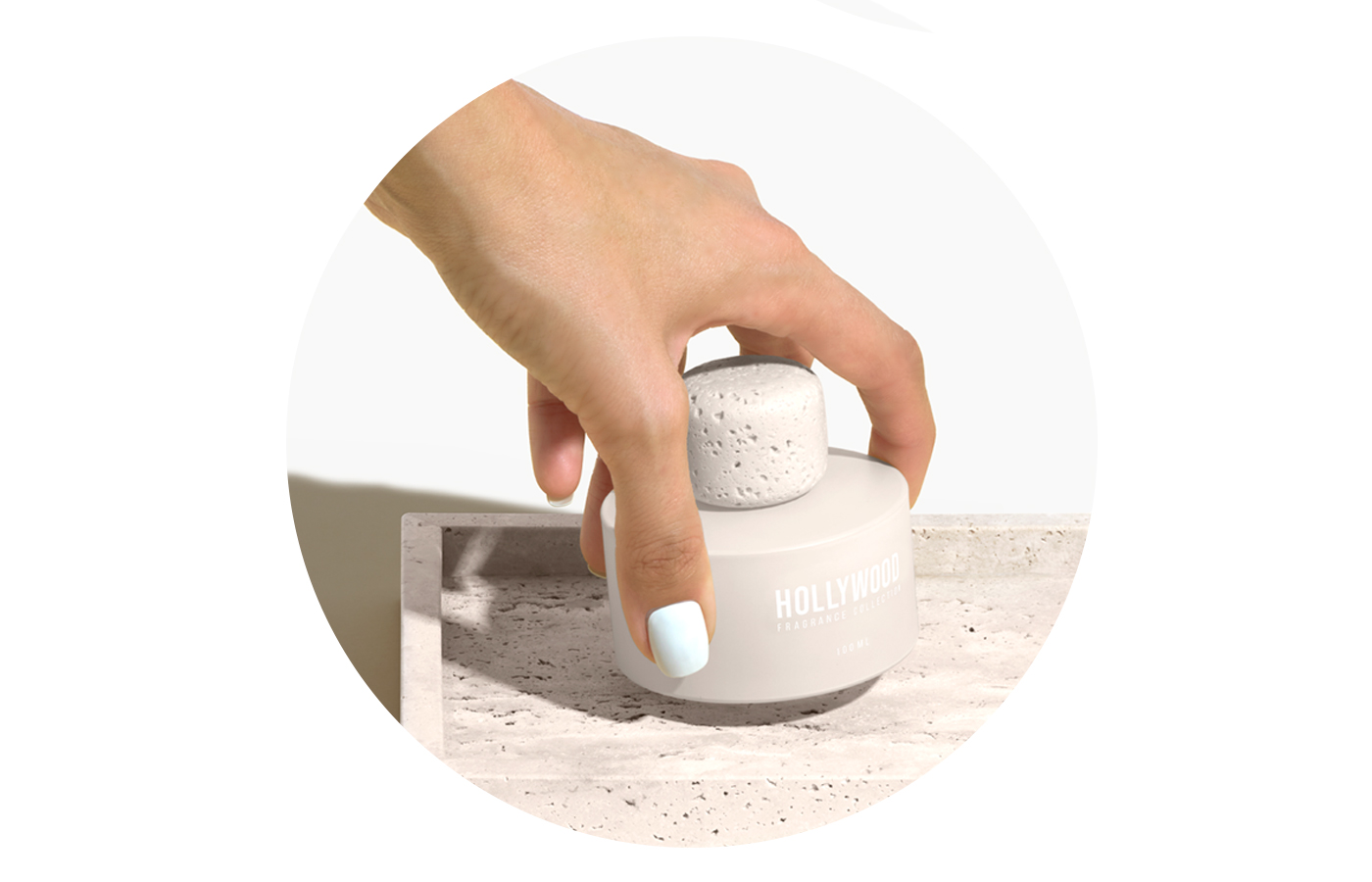 BP_EM_INTERNATIONAL_NEWS_HOLLYWOOD_STEP3 Hand holding a minimalist perfume bottle from Hollywood Fragrance Collection with a textured stone cap, placed on a light marble surface. Luxury fragrance design concept.
