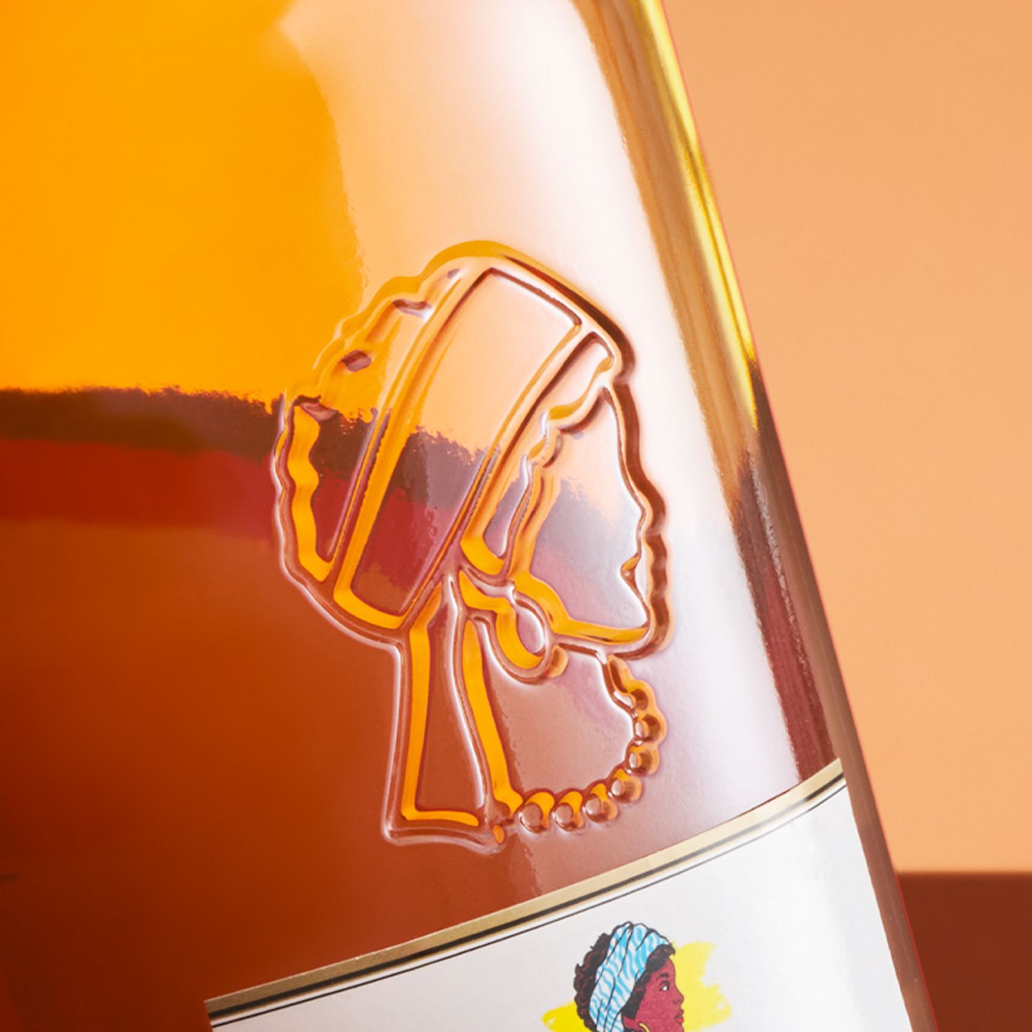 A close-up of Bardinet Negrita rhum bottle with an embossed silhouette of a person's profile, adorned with a headscarf and necklace, against an orange background.