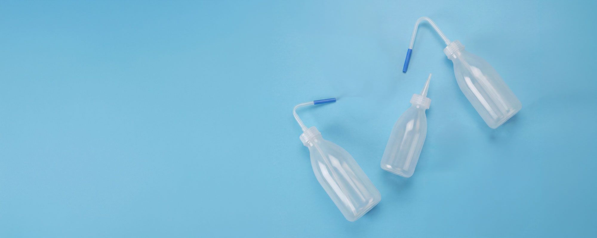 Three transparent plastic bottles with angled spouts and blue caps on a light blue background.