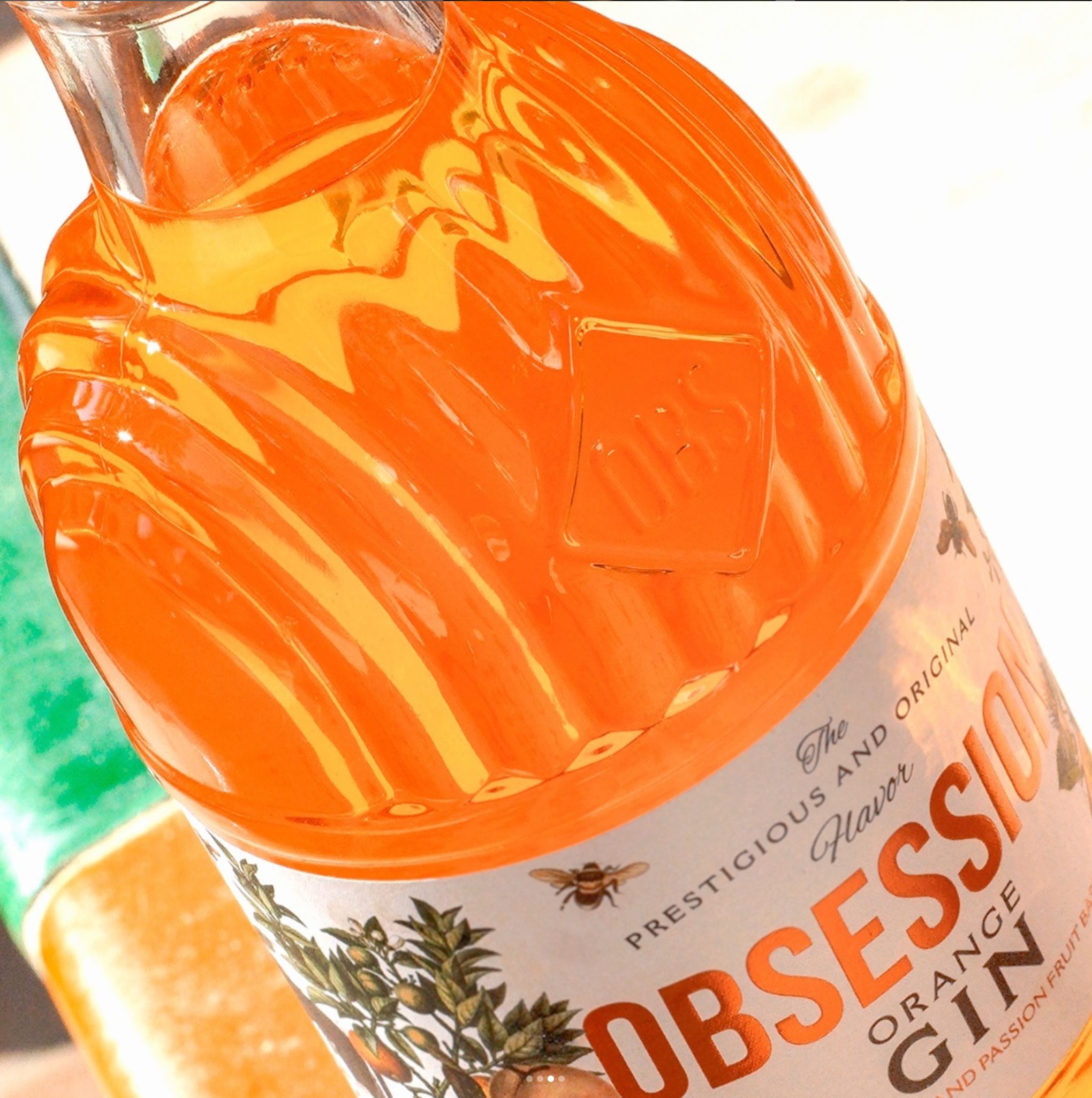 Detailed view of an orange Obsession Gin bottle highlighting the embossed OBS logo on the customized glass design and part of the botanical-themed label.
