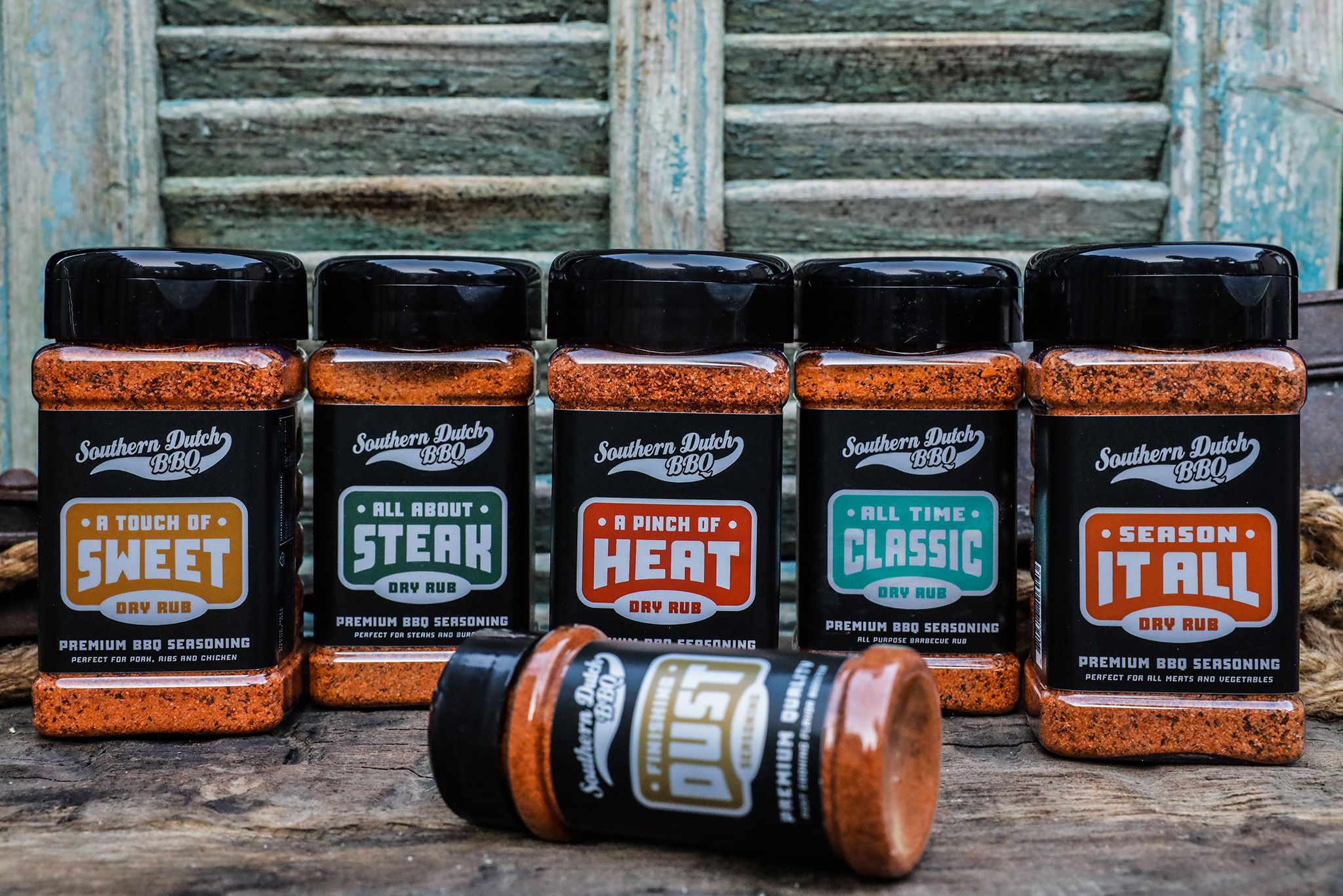 Five jars of Southern Dutch BBQ seasoning, labeled as sweet, steak, heat, classic, and all-purpose varieties, with one jar lying in the foreground.