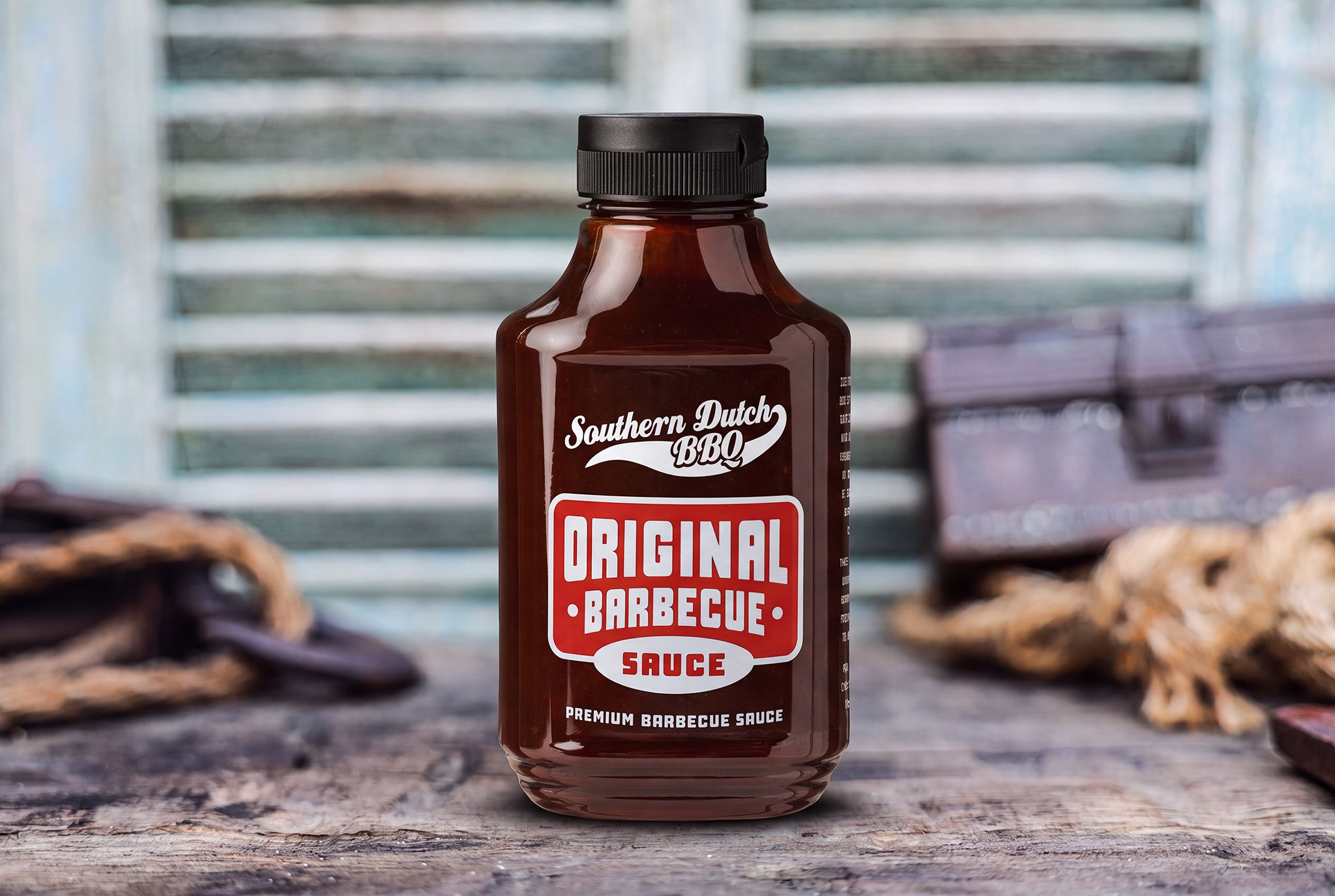 A bottle of Southern Dutch BBQ Original Barbecue Sauce on a rustic wooden surface, with a blurred wooden background and rope.