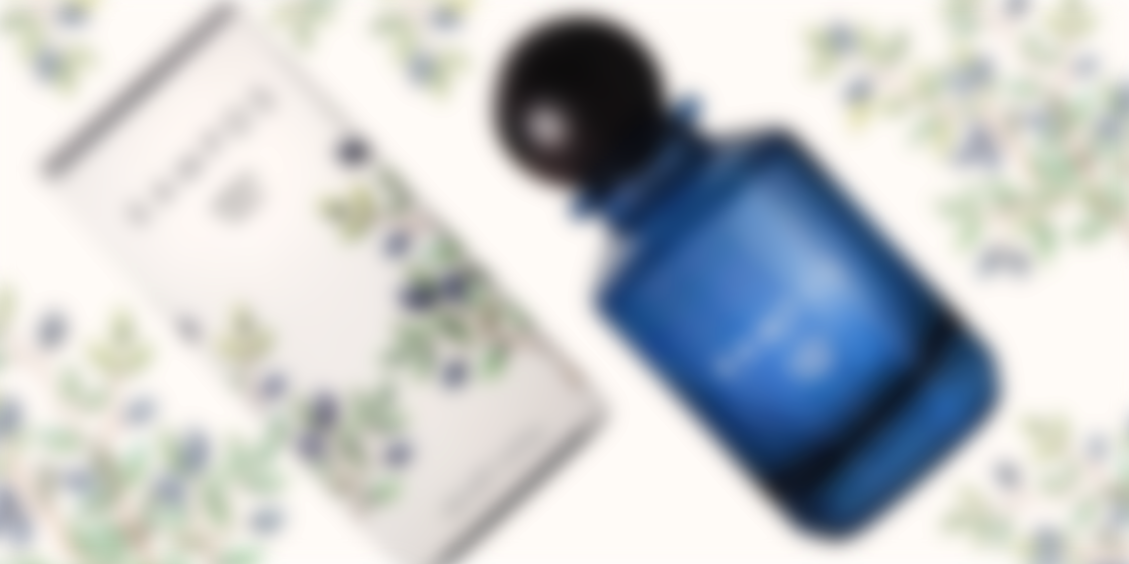 Blue glass perfume bottle labeled 'KAMPOS MYRTLE Parfum' placed next to its white packaging box decorated with green leaves and dark berries on a light background.