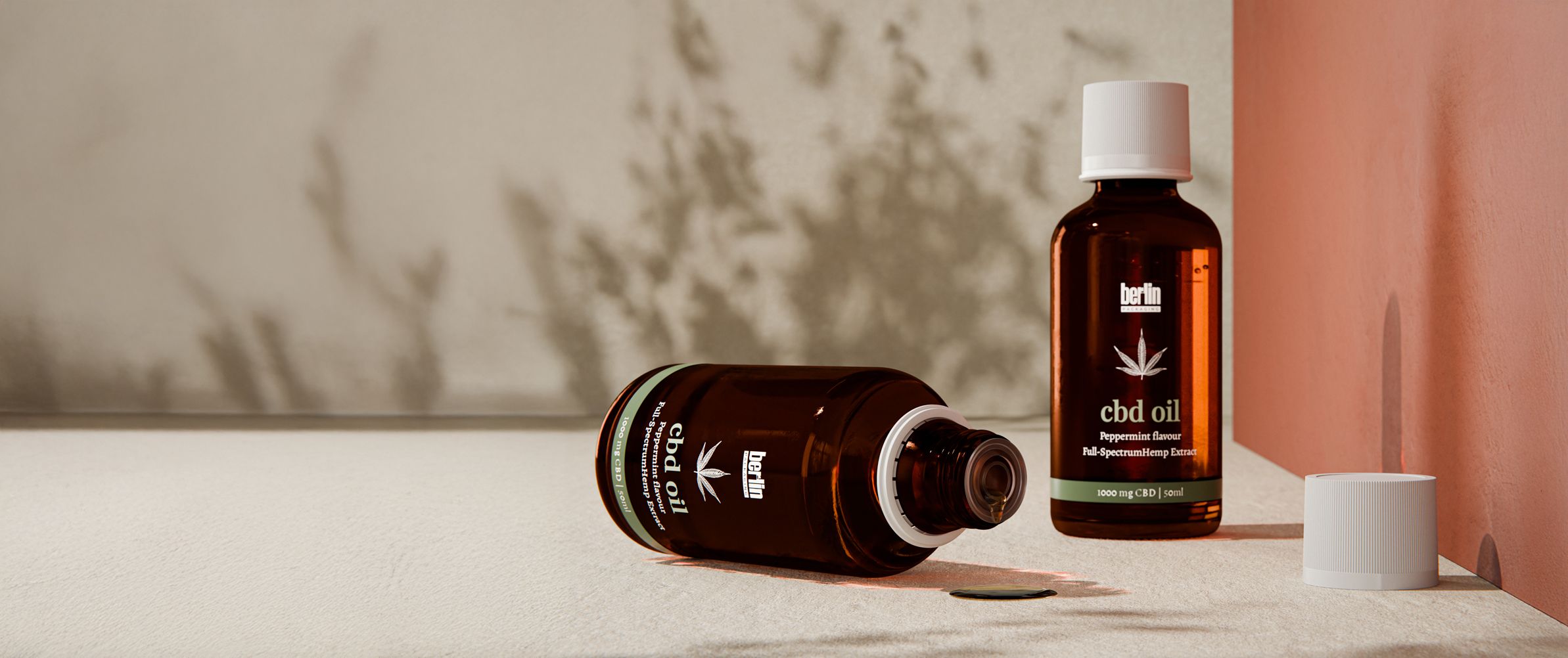 Two amber glass bottles of Berlin CBD oil with peppermint flavor, one standing and one lying down with cap removed, displayed on a beige surface against a warm-toned background