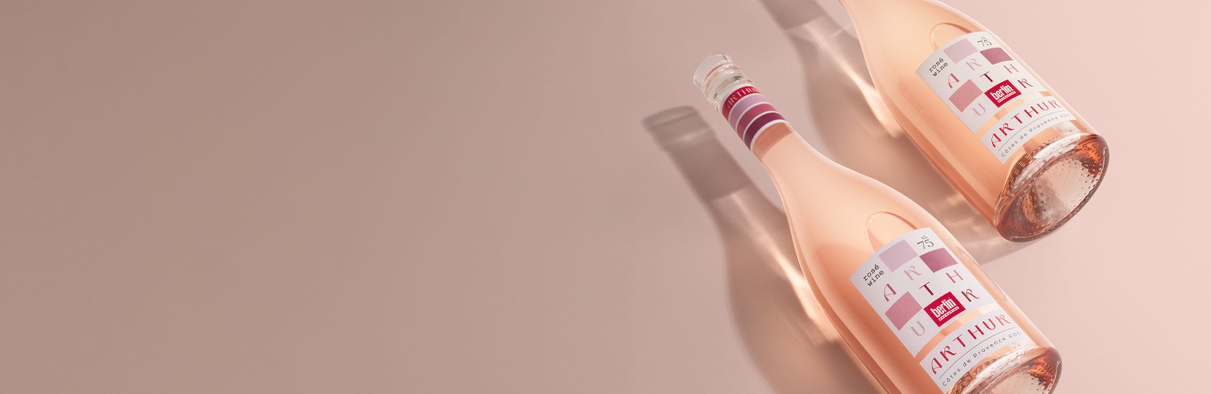 Two bottles of Arthur for rosé wine on a pink surface, with soft lighting and shadows highlighting the elegant design.