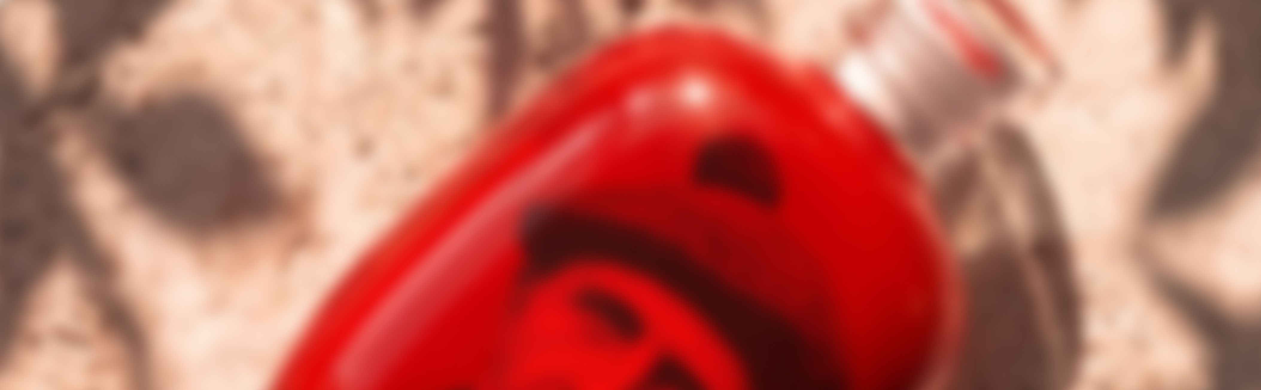 A blurred image of Stone bottle by Berlin Packaging for Camugin with red sleeve and black design, placed on a textured surface with shadows.