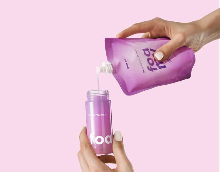 Flexible packaging solution by Berlin Packaging Beauty pouring liquid into Foamy glass foamer bottle, demonstrating easy refill process and sustainable hand soap packaging system.