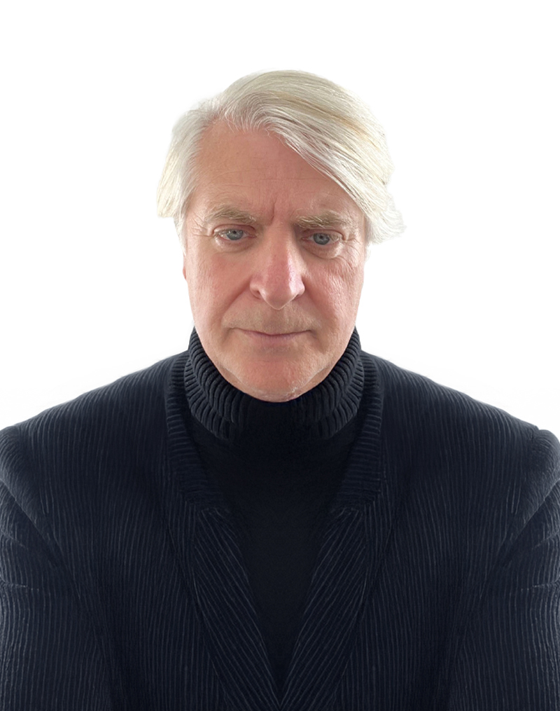 Elderly man with white hair wearing a black turtleneck and jacket, posing against a plain white background.