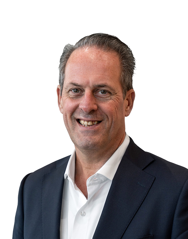 Smiling man with short gray hair, wearing a dark suit and a white shirt, against a plain white background.