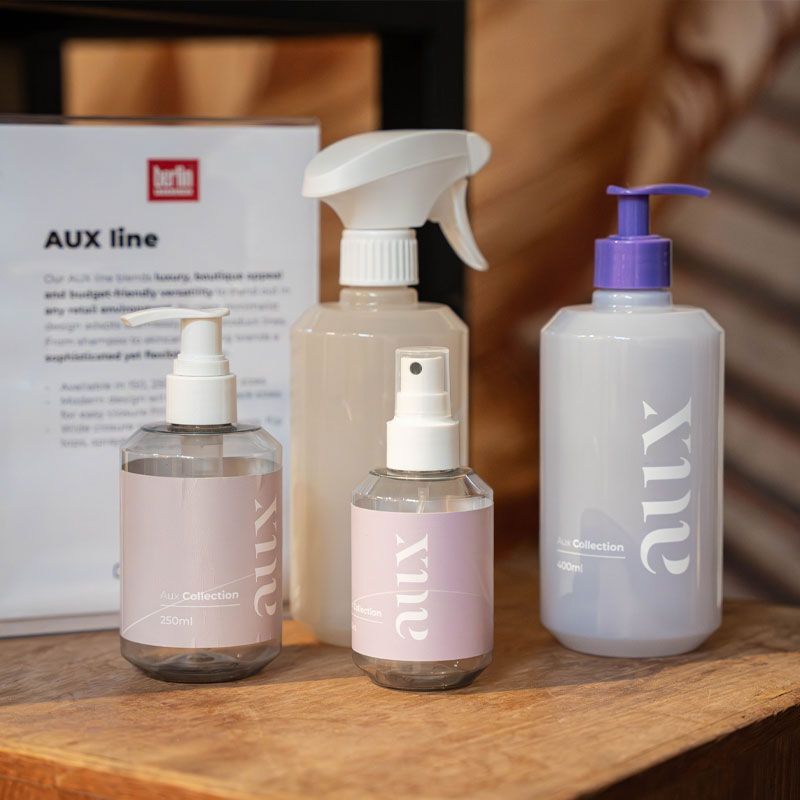Four AUX line bottles with various dispensers displayed on a wooden surface, featuring a label with product information in the background.