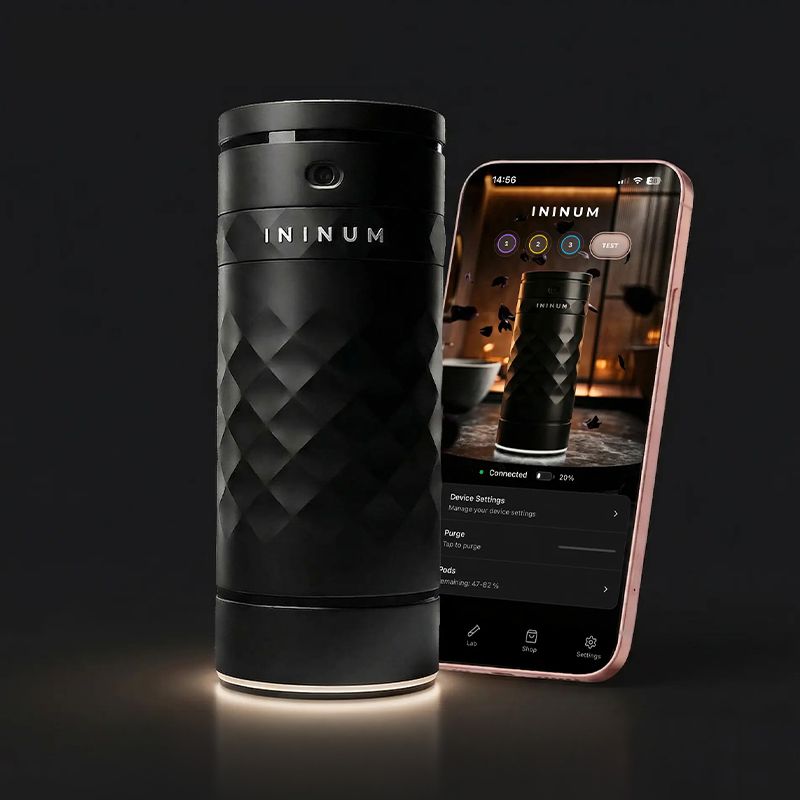 Ininum smart fragrance device by Berlin Packaging Beauty displayed next to mobile app interface, featuring a faceted black design and connected technology for personalized fragrance experiences.