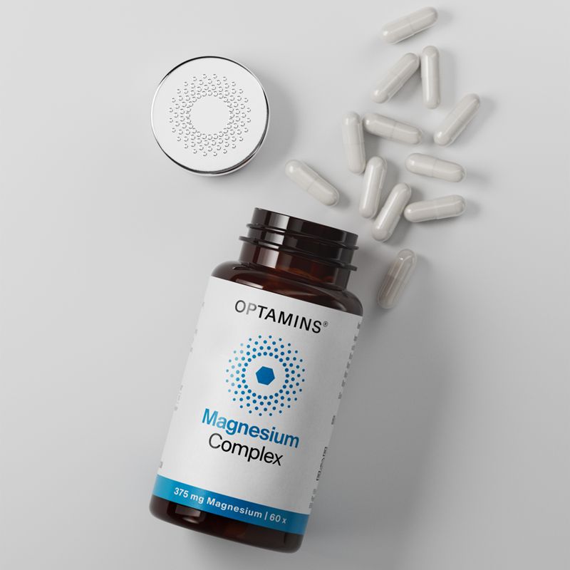 A bottle labeled "Optamins Magnesium Complex" lies open with white capsules scattered around. The lid displays a circular dotted pattern.