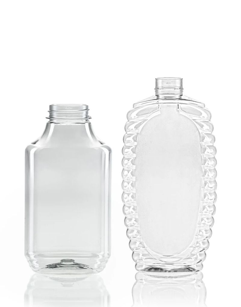 Two clear, empty bottles on a white background; one with a rectangular shape, the other oval with a decorative textured edge.