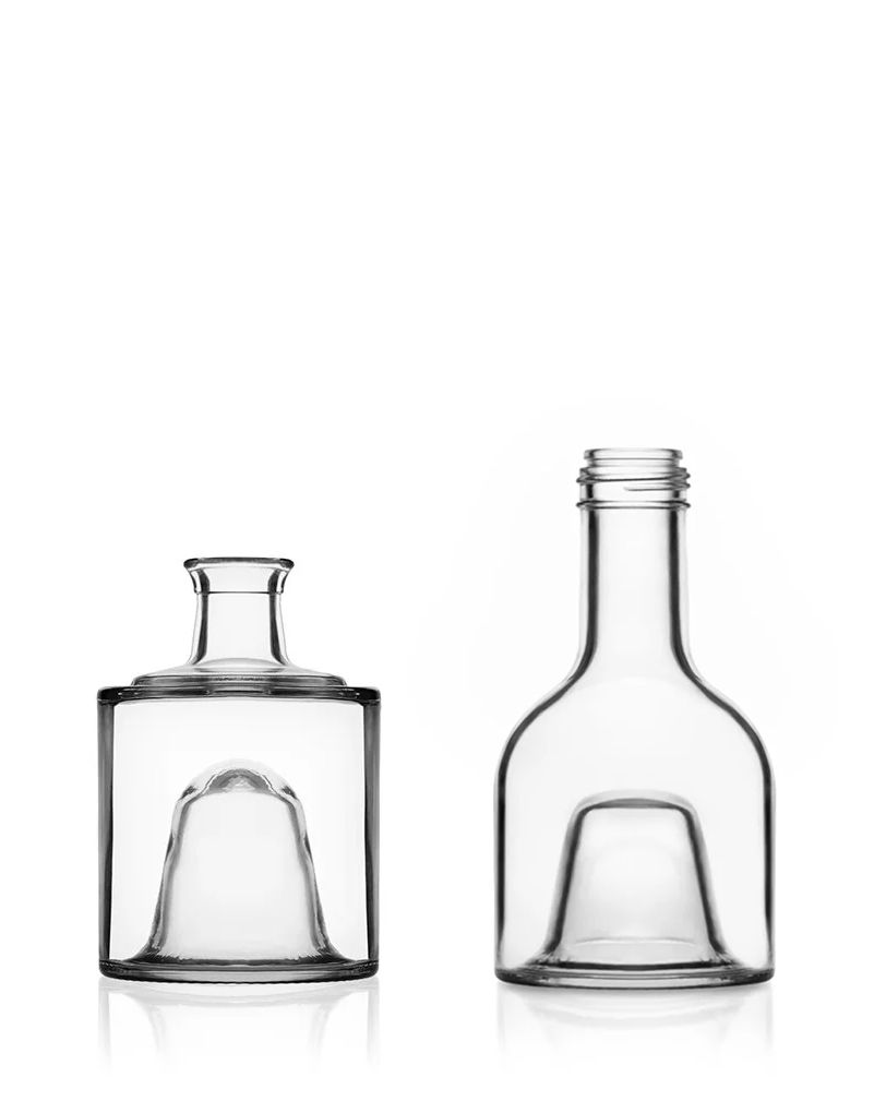 Two empty, clear glass bottles with unique contours on a white background, one with a short neck and the other taller with a threaded top.