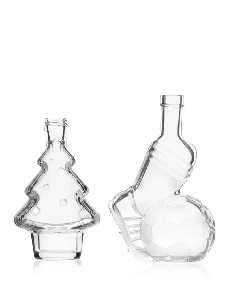 other_glass_bottles Two clear glass bottles shaped like a Christmas tree and a soccer ball with a shoe, standing against a white background.