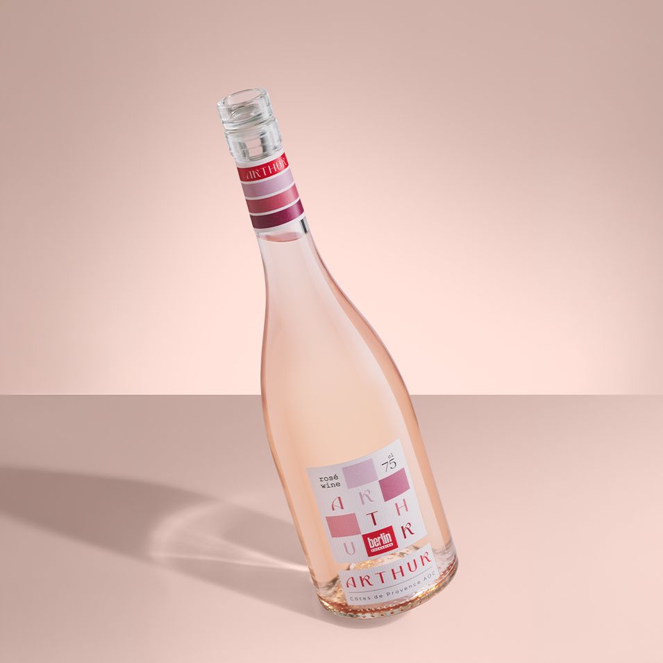 A tilted Arthur bottle by Berlin Packaging filled with rosé wine with a pink and white label featuring geometric designs on a soft pink background.