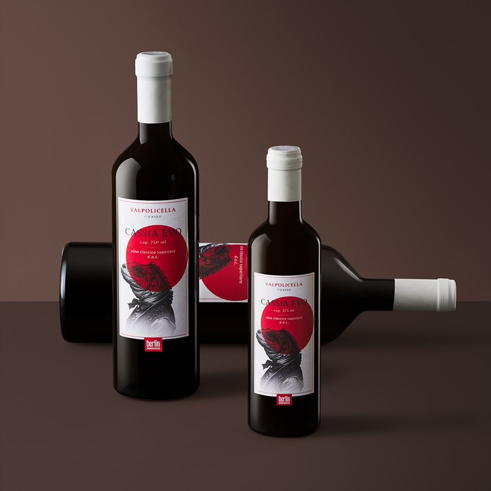 three bottle of Cassia Evo by Berlin Packaging, two standing and one lying down, featuring elegant labels with a red and black design on a dark background.