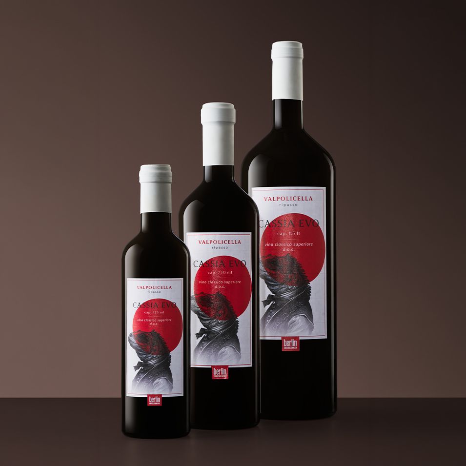 Three bottles Cassia Evo by Berlin Packaging with white labels featuring red and black abstract designs, placed against a dark gradient background.