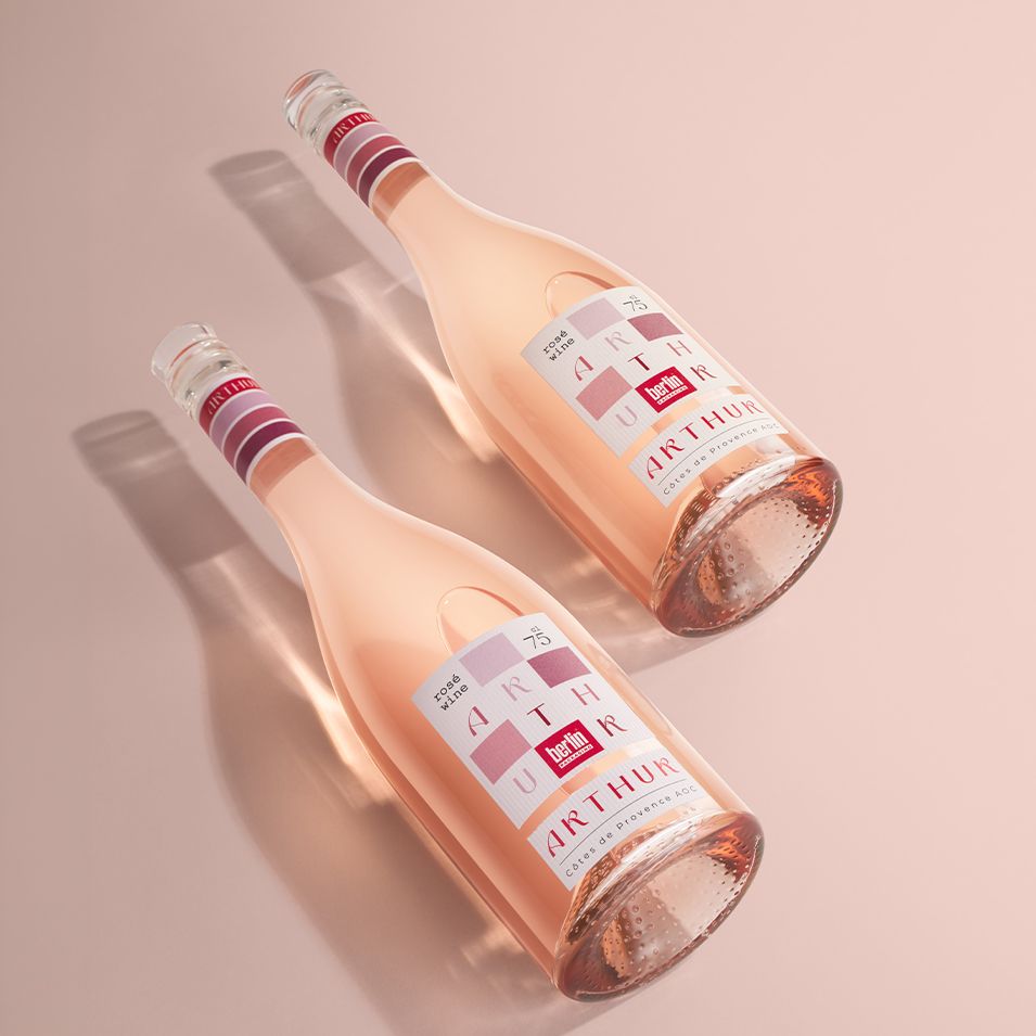 Two Arthur bottles by Berlin Packaging of rosé wine, with pink and white accents, lying on a pastel pink surface.