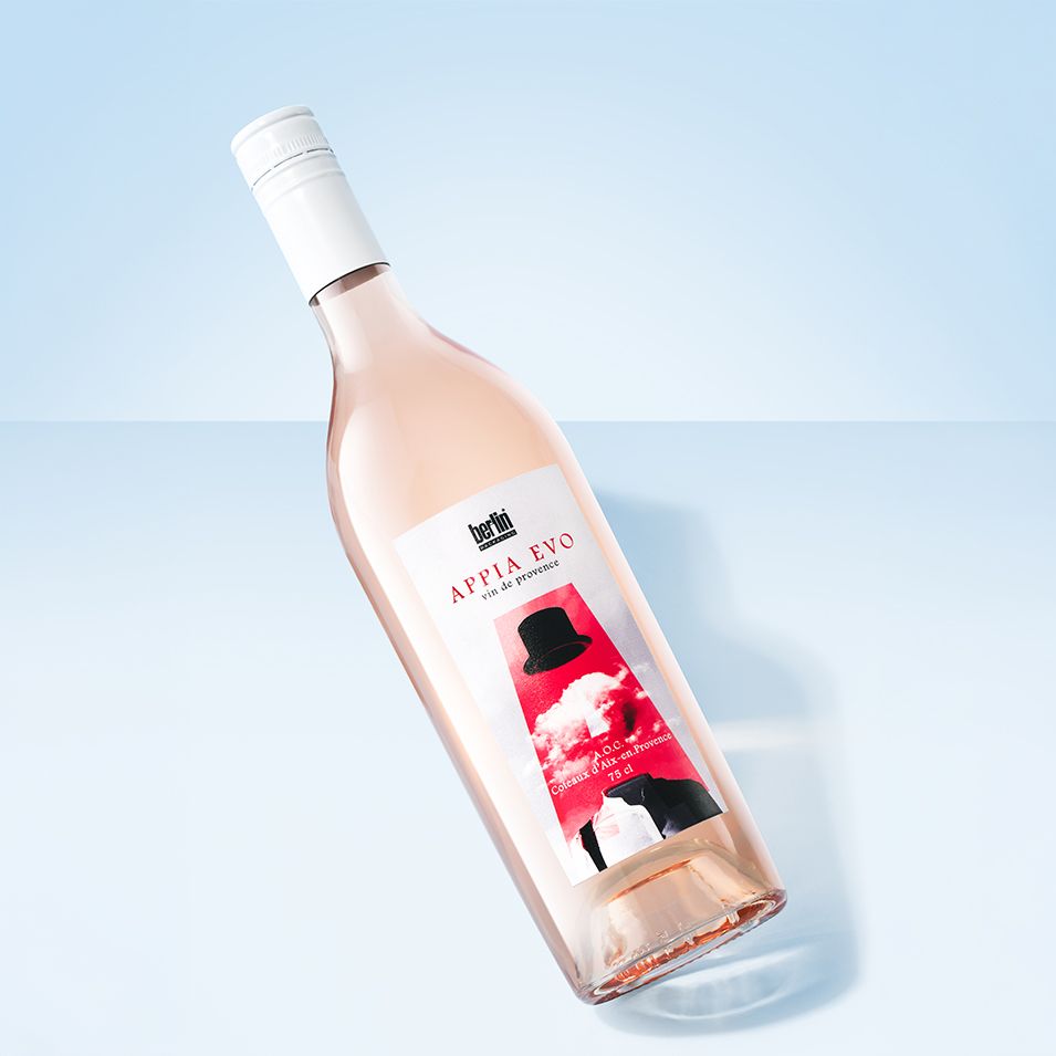 Appia Evo bottle by Berlin Packaging filled with rosé wine with a white cap and artistic label, set on a light blue background.
