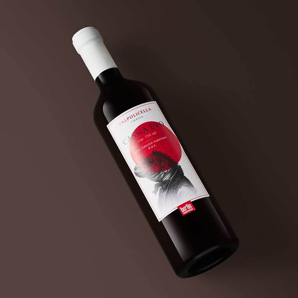 A bottle Cassia Evo by Berlin Packaging with a white label featuring an artistic design and text, set on a dark brown background.