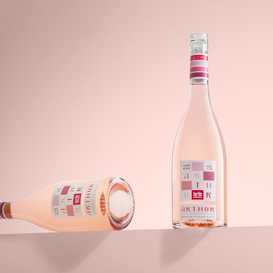 Two elegant Arthur bottles by Berlin Packaging filled with rosé wine against a soft pink background, one standing upright and the other lying on its side.