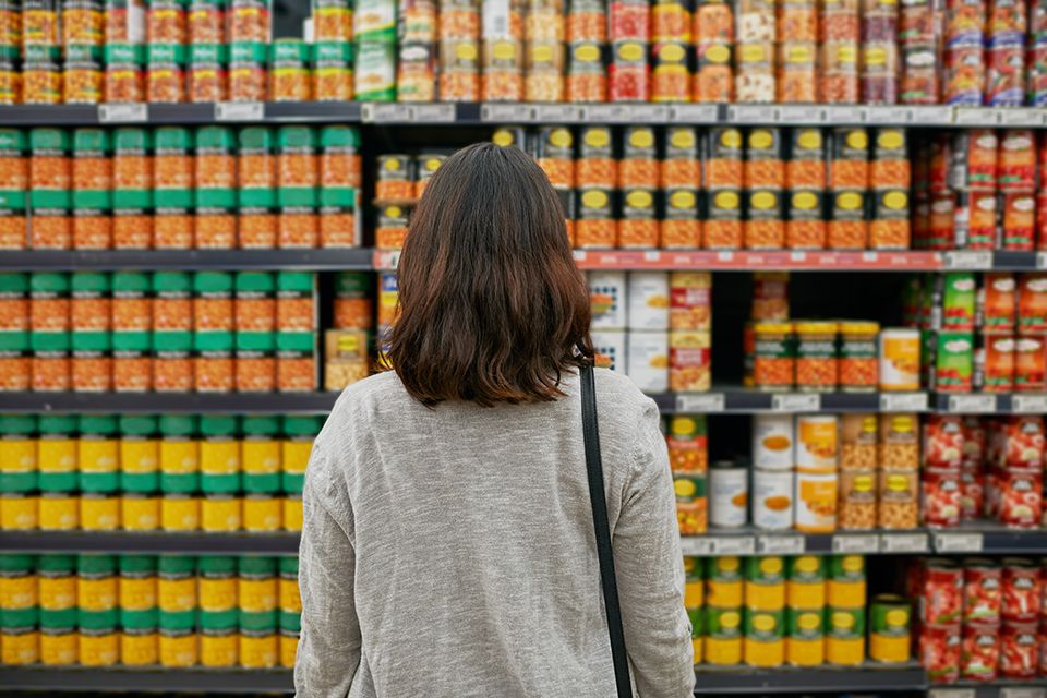 Woman browsing canned food aisle in supermarket with shelves full of colorful packaged goods