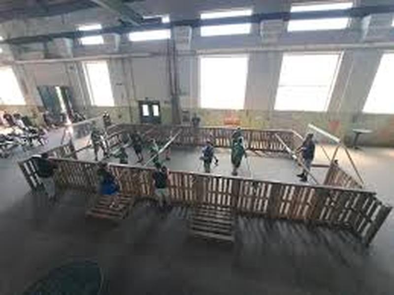 Indoor-Spielfeld mit Holzbarrieren; Personen spielen ein Spiel, während große Fenster den Raum mit Licht durchfluten