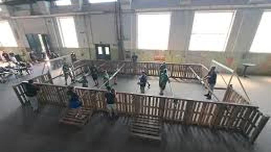 Indoor-Spielfeld mit Holzbarrieren; Personen spielen ein Spiel, während große Fenster den Raum mit Licht durchfluten