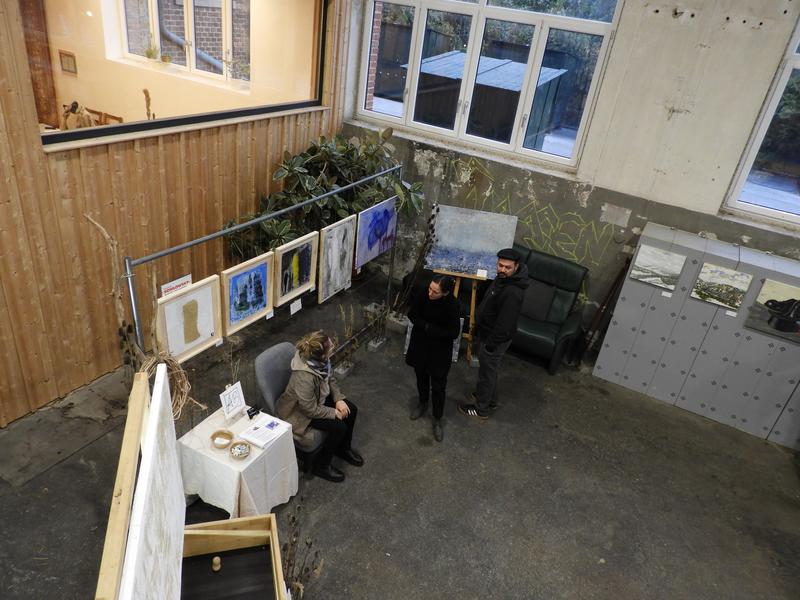 Kunstausstellung mit gerahmten Gemälden auf Ständern in gedämpftem Licht; eine Person betrachtet die Kunstwerke