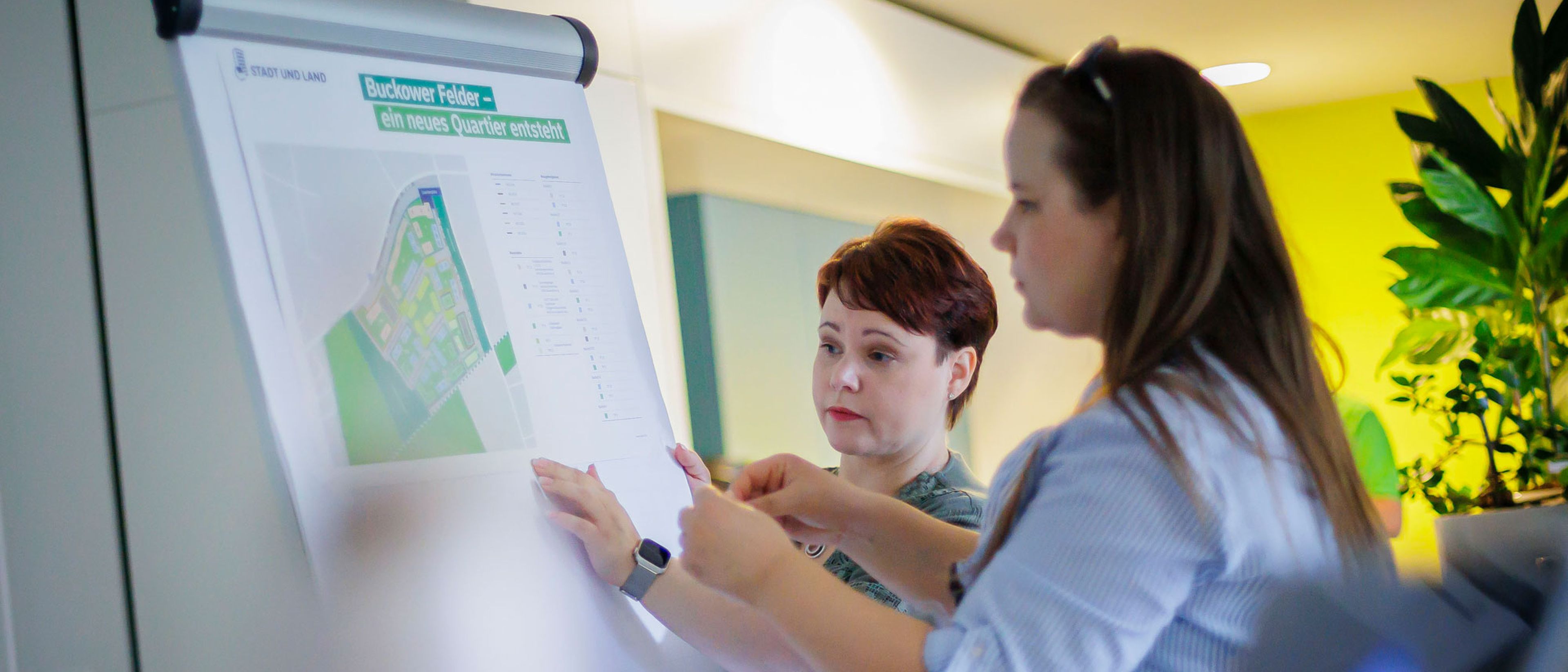 Zwei Frauen hängen ein Poster mit Informationen zusammen auf
