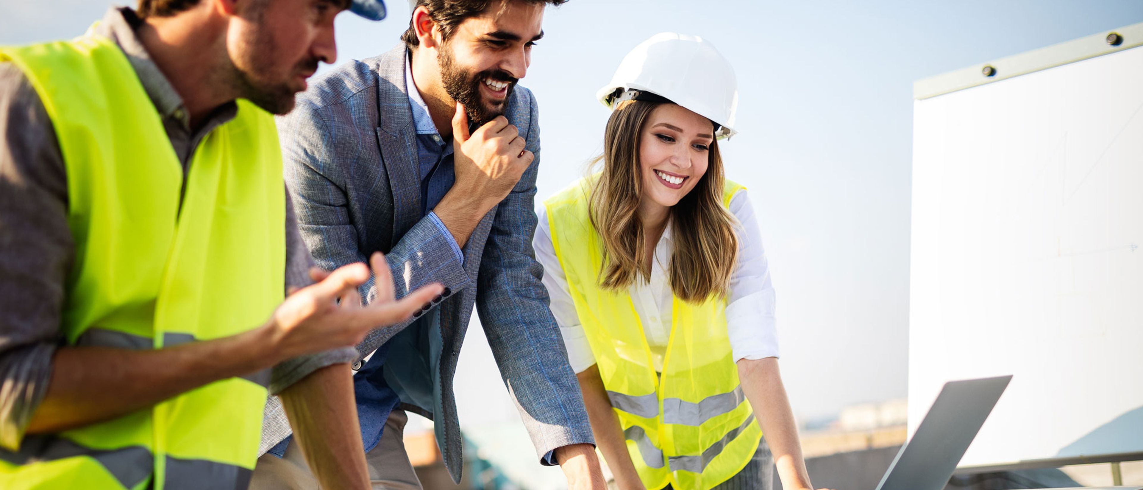 Drei Personen diskutieren miteinander und stehen vor einem Computer auf einer Baustelle