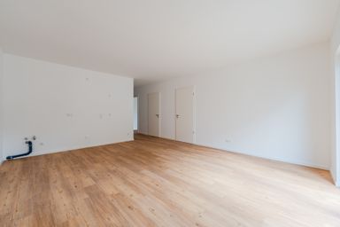 Empty room with light wooden flooring, white walls, two closed doors, and plumbing fixtures visible on one wall.