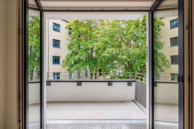 Open balcony with metal railing looks out onto a building and lush green trees.