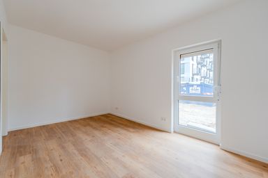 Empty room with white walls, wooden floor, and a window showing a view of a construction site outside.