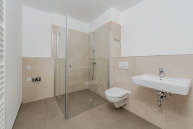 Modernes Badezimmer mit bodengleicher Dusche, WC und Waschbecken, beige Fliesen an Wand und Boden.
