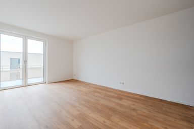 Leerer Raum mit Holzfußboden und weiß gestrichenen Wänden, Blick auf Balkon durch große Fenster.