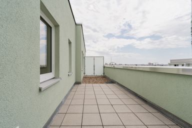 Blick auf eine geräumige Dachterrasse mit grünen Wänden und Fliesenboden, unter einem bewölkten Himmel.