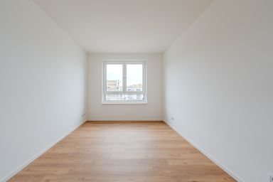 Leerer, heller Raum mit Holzfußboden und einem Fenster, das auf eine städtische Umgebung blickt.