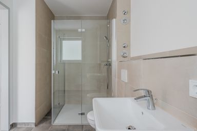 Modern bathroom with a glass-enclosed shower, beige tiles, chrome fixtures, and a white sink with a sleek faucet.