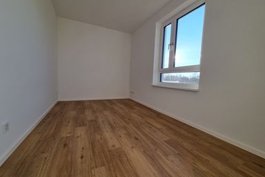 Ein leerer Raum mit Holzfußboden und einem großen Fenster, das Tageslicht hereinlässt.