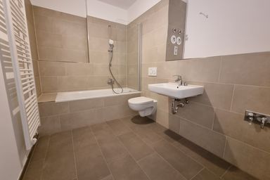 Modernes Badezimmer mit Badewanne, Wanddusche, Waschbecken und Toilette. Beige Fliesen und Handtuchheizkörper an der Wand.
