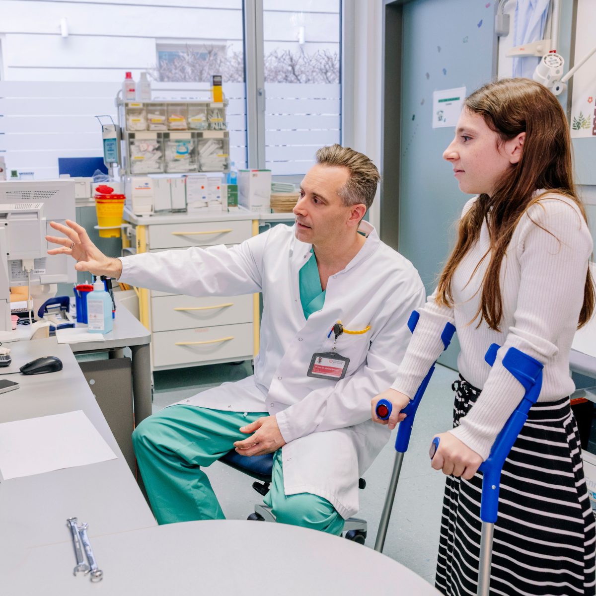 Arzt zeigt jungem Mädchen mit Krücken etwas am Bildschirm